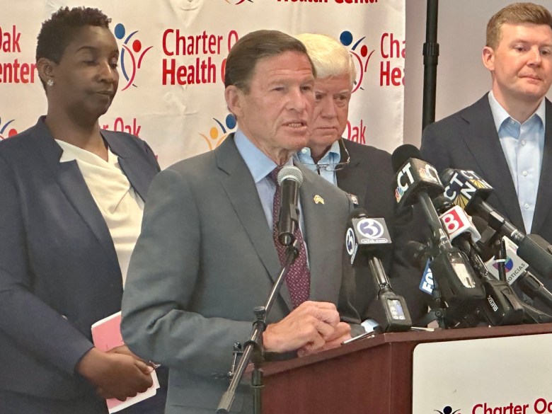 Man in gray suit speaking into microphones