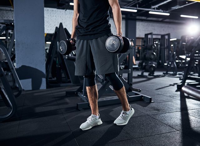 Cropped photo of a sportsman in shorts and white boots walking away with hand weights