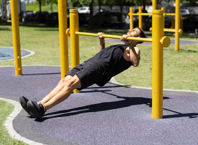 Young man performing inverted rows on outdoor bars. Body weight rows.