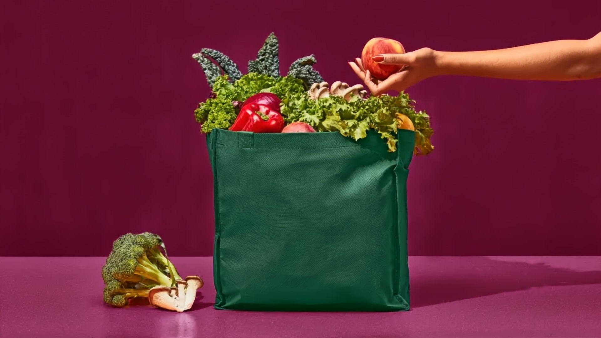 Someone putting a fruit into a green bag on a purple background.