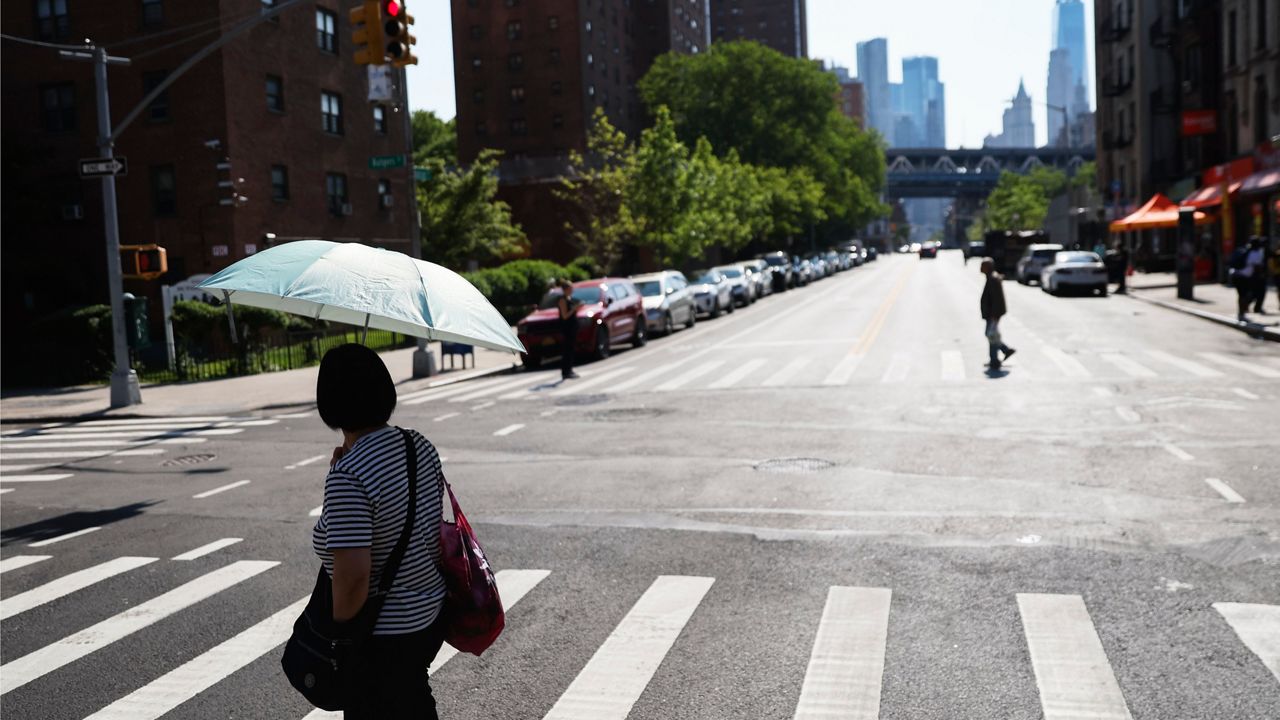 A pedestrian shields themselves from the sun as they cross the street on June 4, 2025, in New York. (AP Photo/Heather Khalifa)