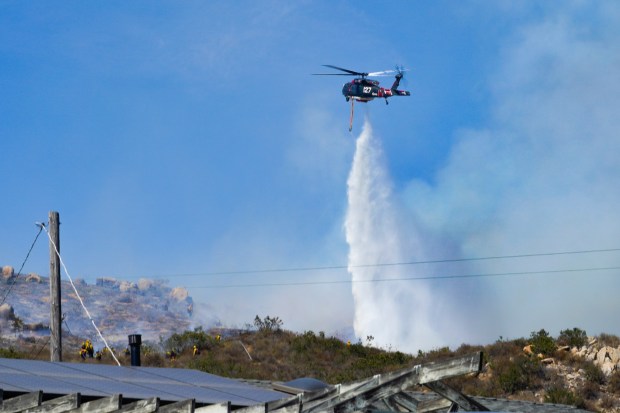 Firefighters are actively working the fire line just north of Star Acres Lane, while a helicopter conducts a water drop during the Steel Fire on Wednesday, July 9, 2025, in Spring Valley, CA. As of 4:30 PM on Wednesday, the fire has burned 28 acres and is currently 25% contained. (Nelvin C. Cepeda / The San Diego Union-Tribune)