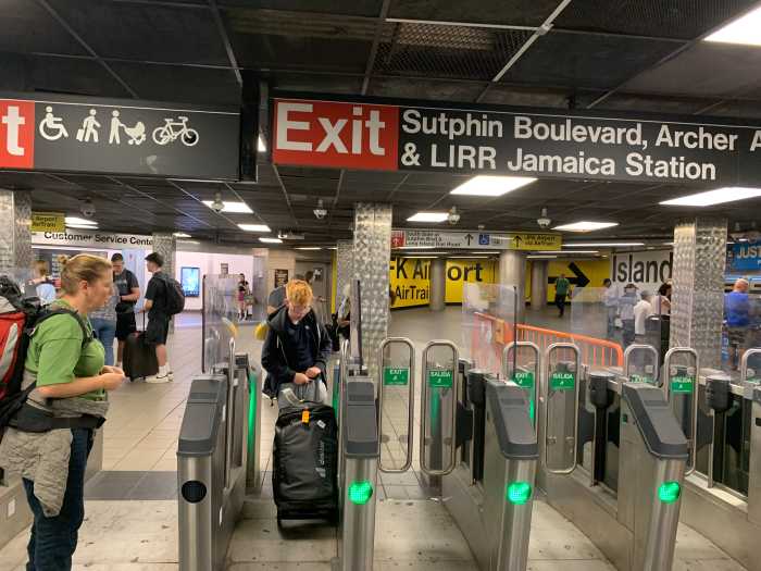 many people, some with luggage, going through turnstiles at a subway station