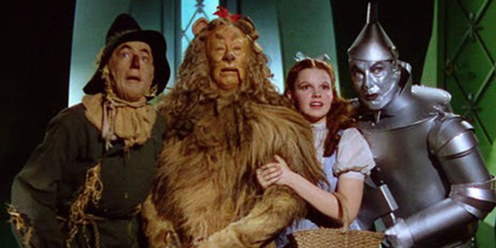 Dorothy Gale, the Scarecrow, the Cowardly Lion, and the Tin Man stand huddled together in The Wizard of Oz movie.