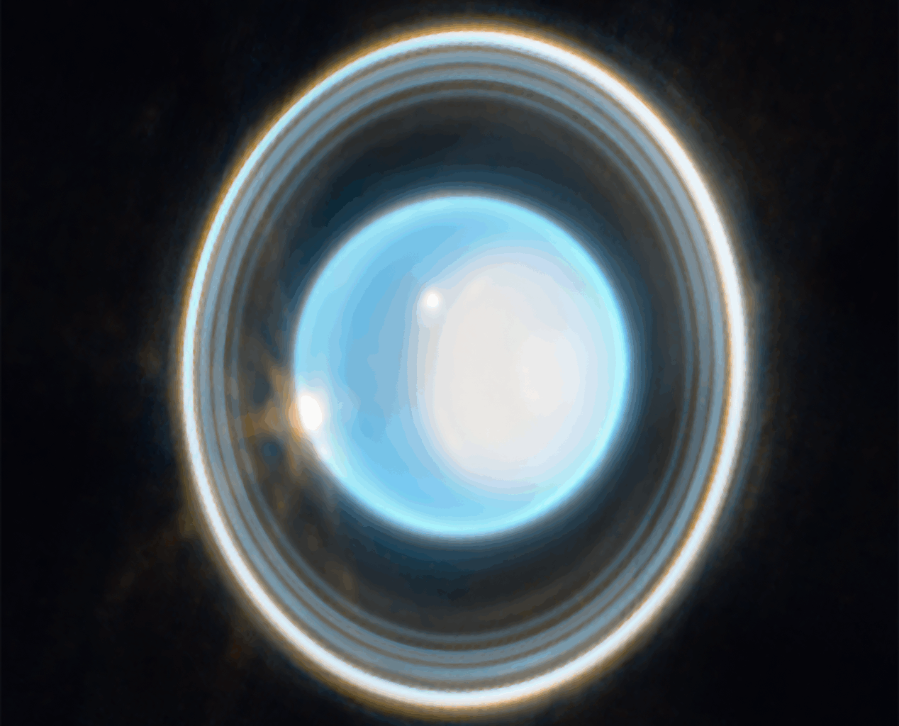 A glowing, bright blue-white circular sphere in the center of the image, surrounded by multiple concentric, thin rings of varying brightness against a black background. The rings appear as gray, white, and light-colored bands encircling the central blue-white disc. The outer ring appears brighter than the inner rings, with subtle variations in thickness and illumination throughout the ring structure.