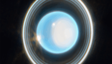 A glowing, bright blue-white circular sphere in the center of the image, surrounded by multiple concentric, thin rings of varying brightness against a black background. The rings appear as gray, white, and light-colored bands encircling the central blue-white disc. The outer ring appears brighter than the inner rings, with subtle variations in thickness and illumination throughout the ring structure.