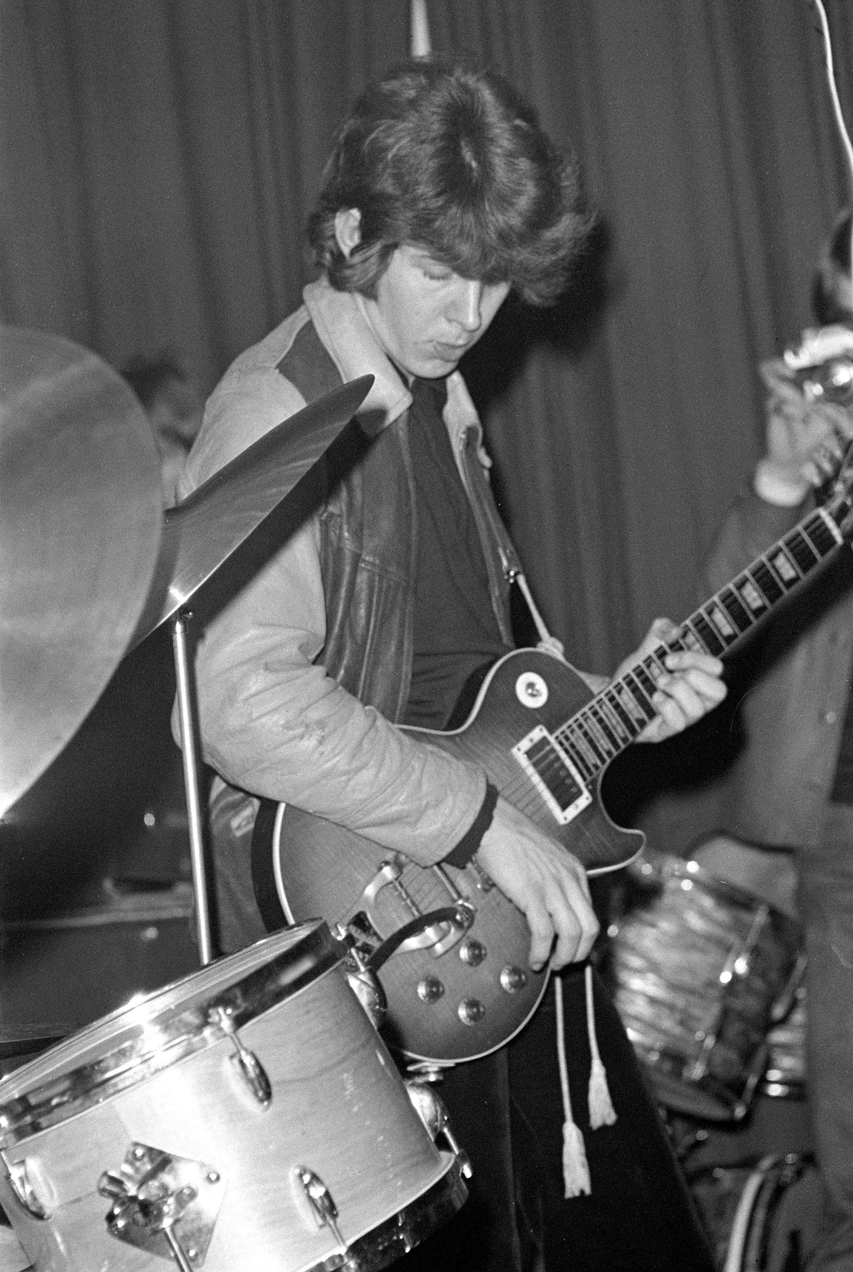 Black and white photo of Mick Taylor playing guitar.