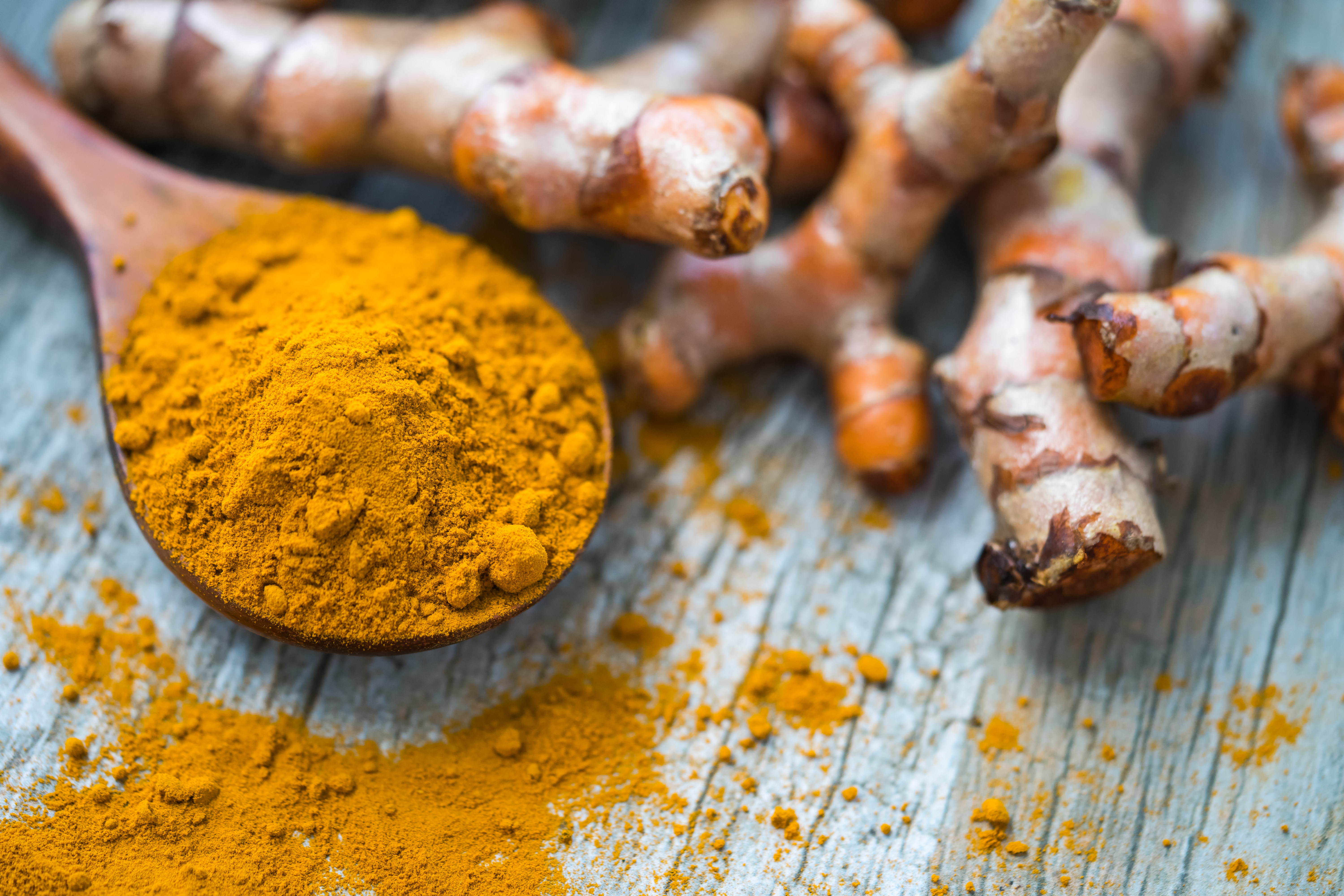 Turmeric powder in a wooden spoon beside fresh turmeric root.