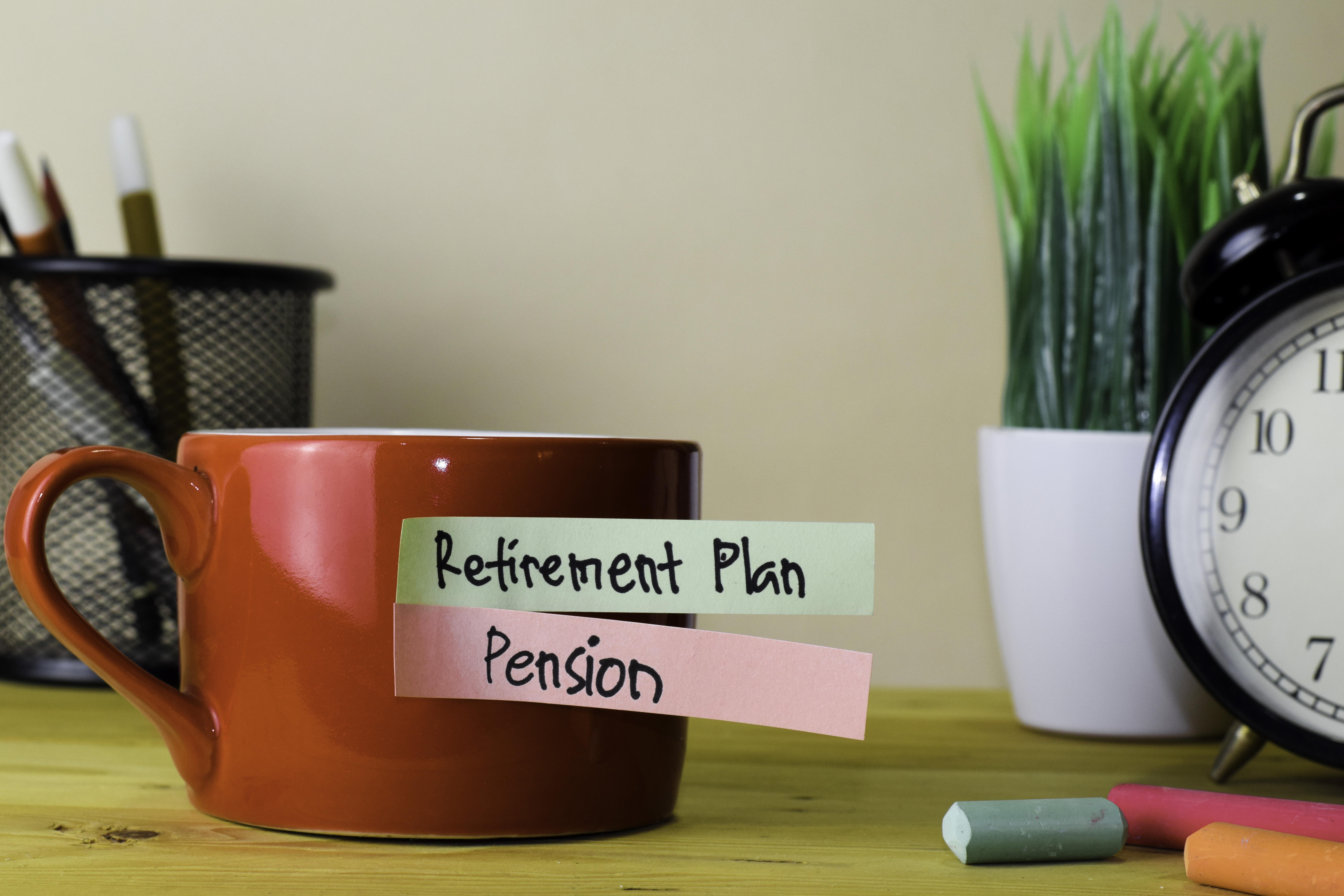 Red mug with sticky notes reading "Retirement Plan" and "Pension."