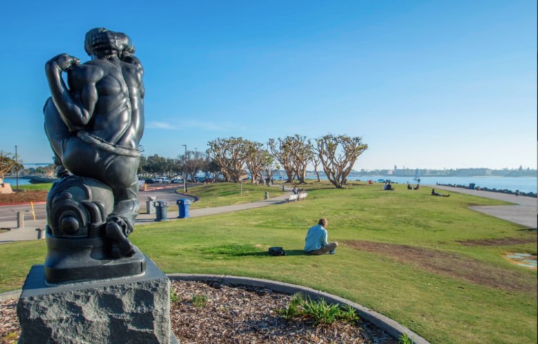 The view past a statue in a park where people sit relaxing on a waterfront.