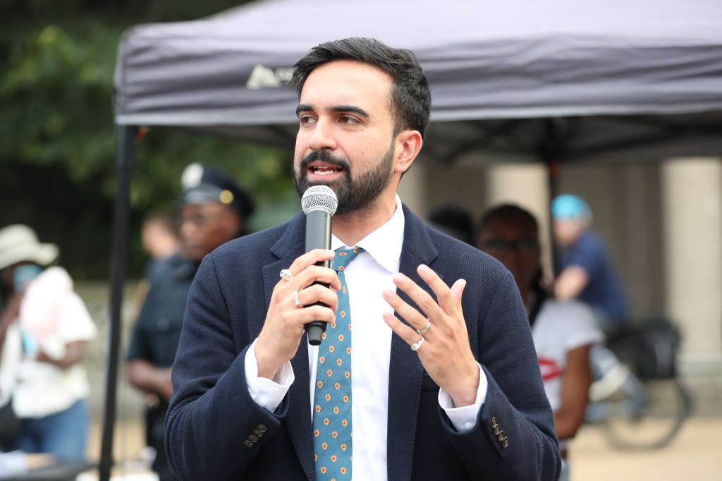 Zohran Mamdani speaking at a microphone.