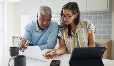 Shot of a senior couple standing in their kitchen going over finances on paper and on a tablet