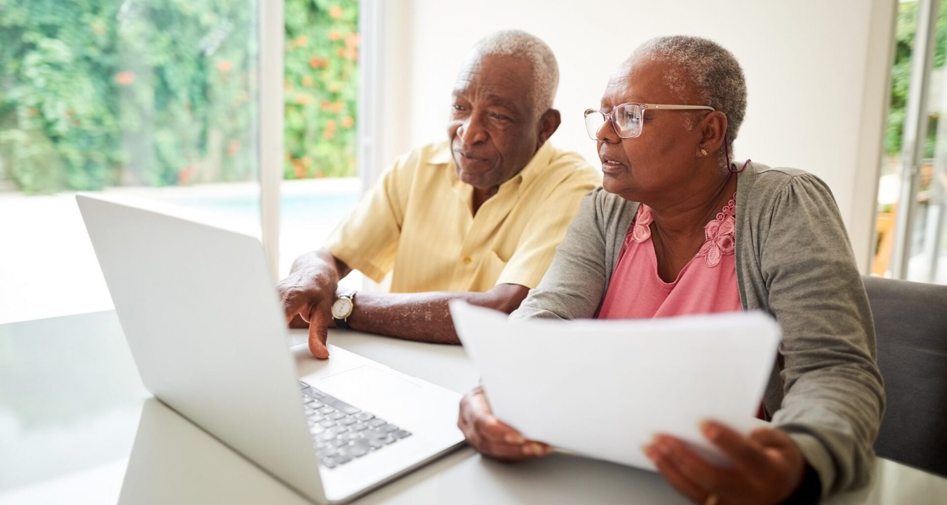 Shot of a senior african couple with a paper looking at a laptop at home.