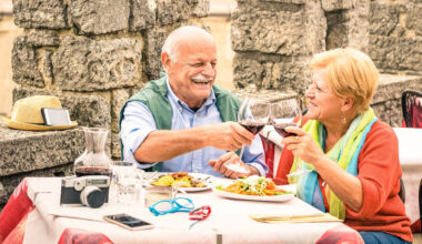 Senior couple having fun and eating at restaurant during travel - Mature man and woman wife in old city town bar during active elderly vacation - Happy retirement concept with retired people together.
