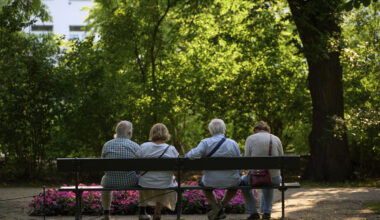 A group of older adults sitting together on a bench, seen from behind.