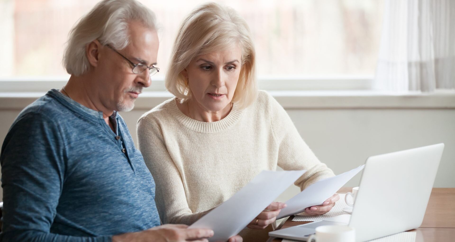 A senior couple looks worried as they read financial statements.