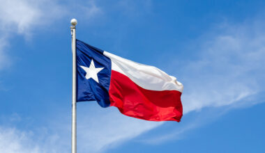 Texas State flag on the pole waving in the wing against blue sky and white clouds.