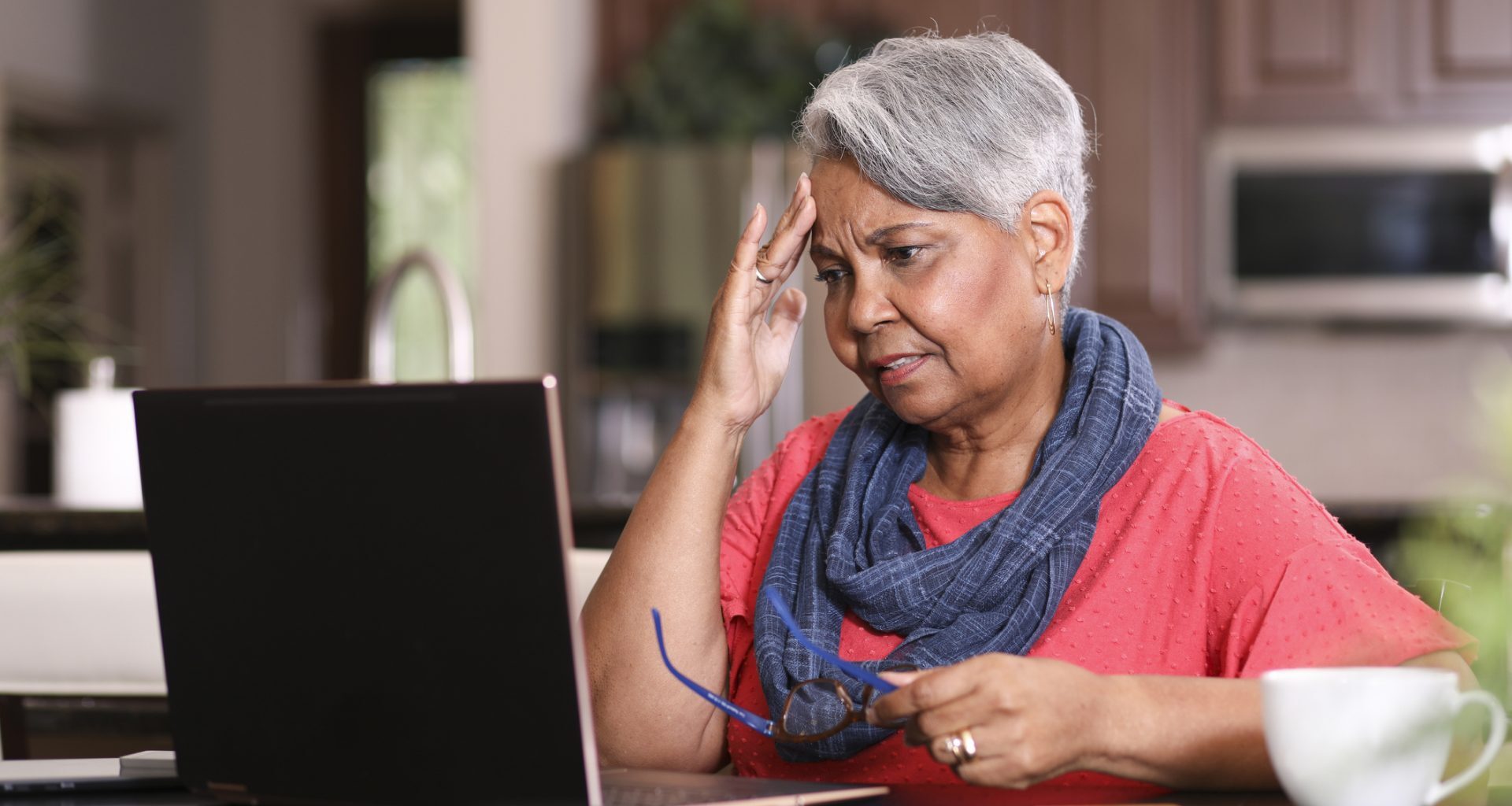 African descent, senior adult woman at home sitting at kitchen table paying bills or online banking using laptop computer.