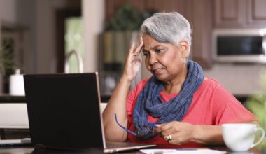 African descent, senior adult woman at home sitting at kitchen table paying bills or online banking using laptop computer.
