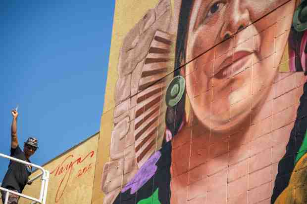 Artist Robert Vargas signs his “Nourishing the Community” mural depicting...