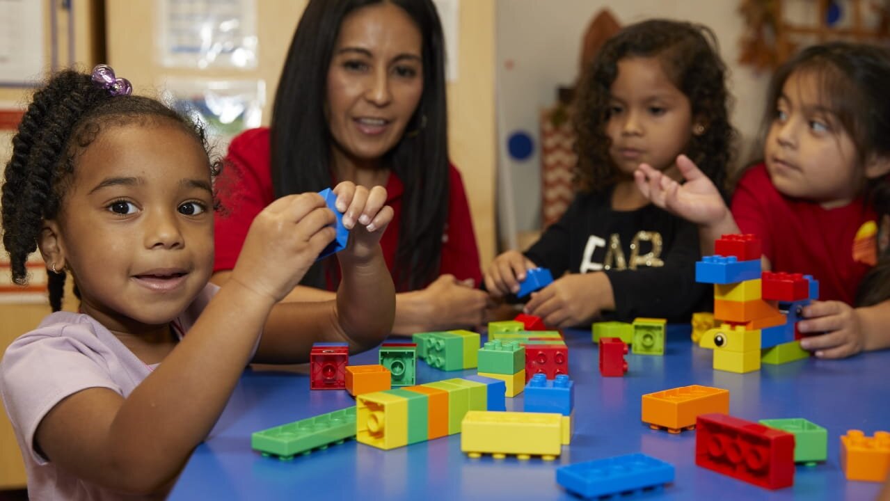 A child care provider sits with children as they play with blocks at a KinderCare facility in Phoenix. KinderCare was selected by the city of Phoenix after a procurement process to be the provider of the child care facility at the 44th Street Sky Train Station for families of workers at Phoenix Sky Harbor International Airport.