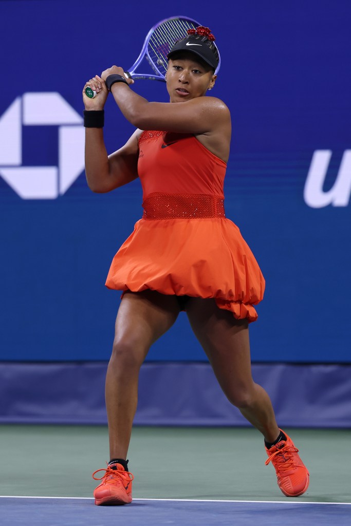 Naomi Osaka returns a serve wearing a red outfit