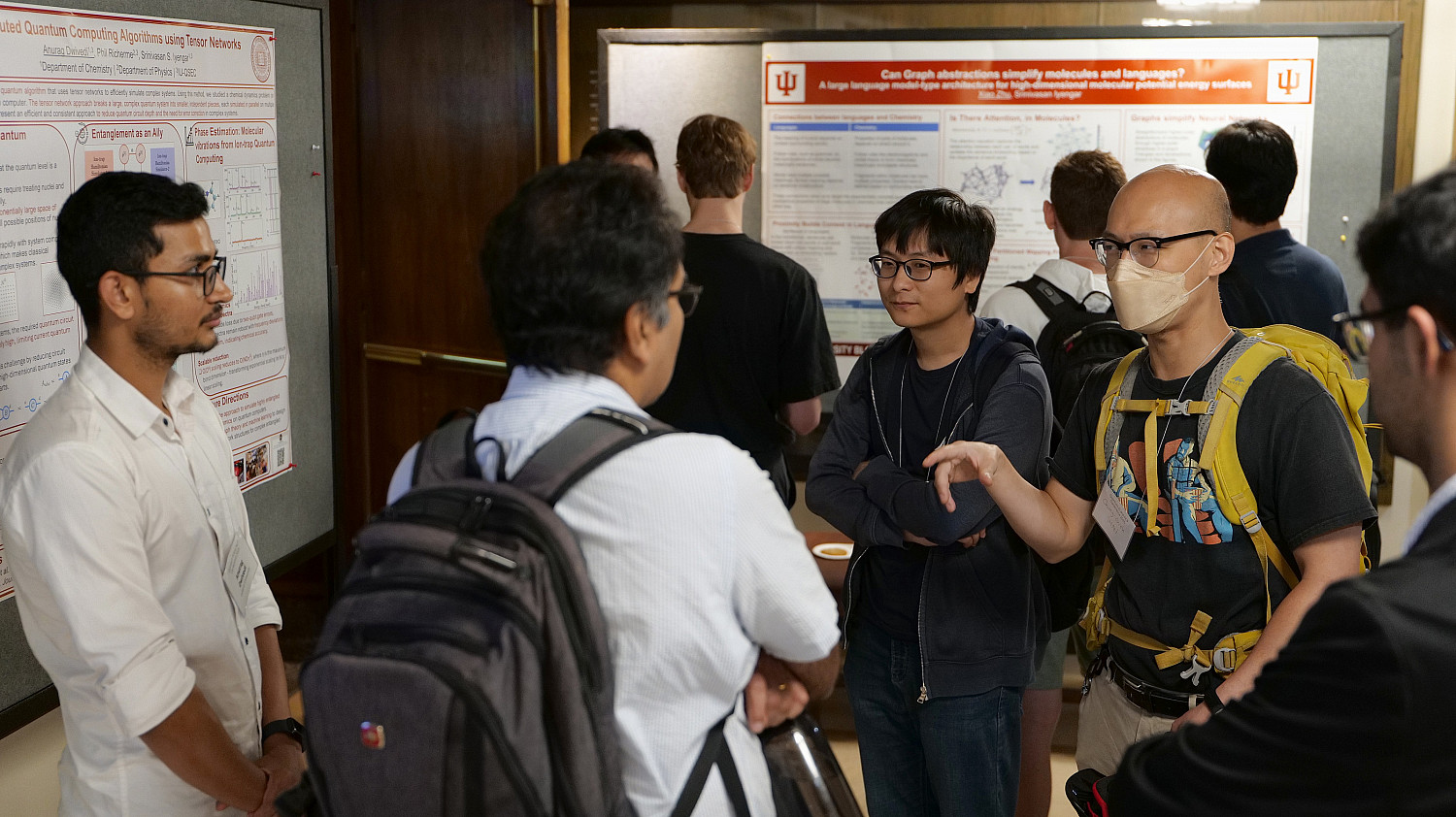 Students, including one wearing glasses and a mask, attend a poster session on Quantum AI.