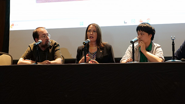 Two men and a woman talk into microphones during a panel discussion.