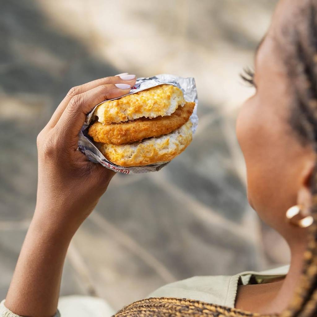 Image shows a woman eating a Chick-fil-A breakfast chicken biscuit.