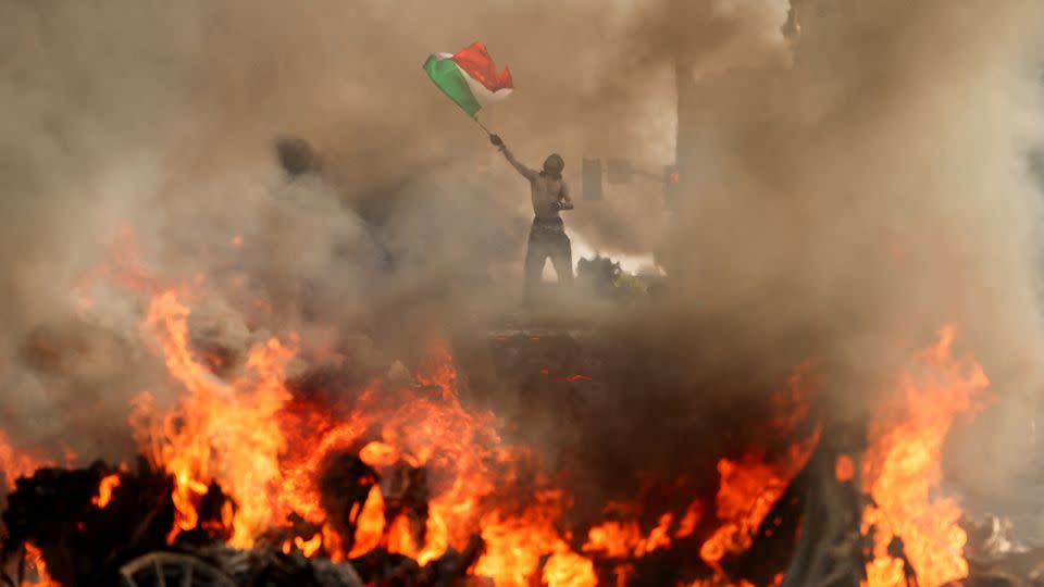 A man waves a Mexican flag as smoke and flames rise from a burning vehicle during a protest against federal immigration sweeps in downtown Los Angeles on June 8. - David Swanson/Reuters