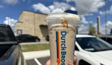 The Golden Eagle, a vanilla and caramel breve with caramel drizzle, being held in front of a Dutch Bros location
