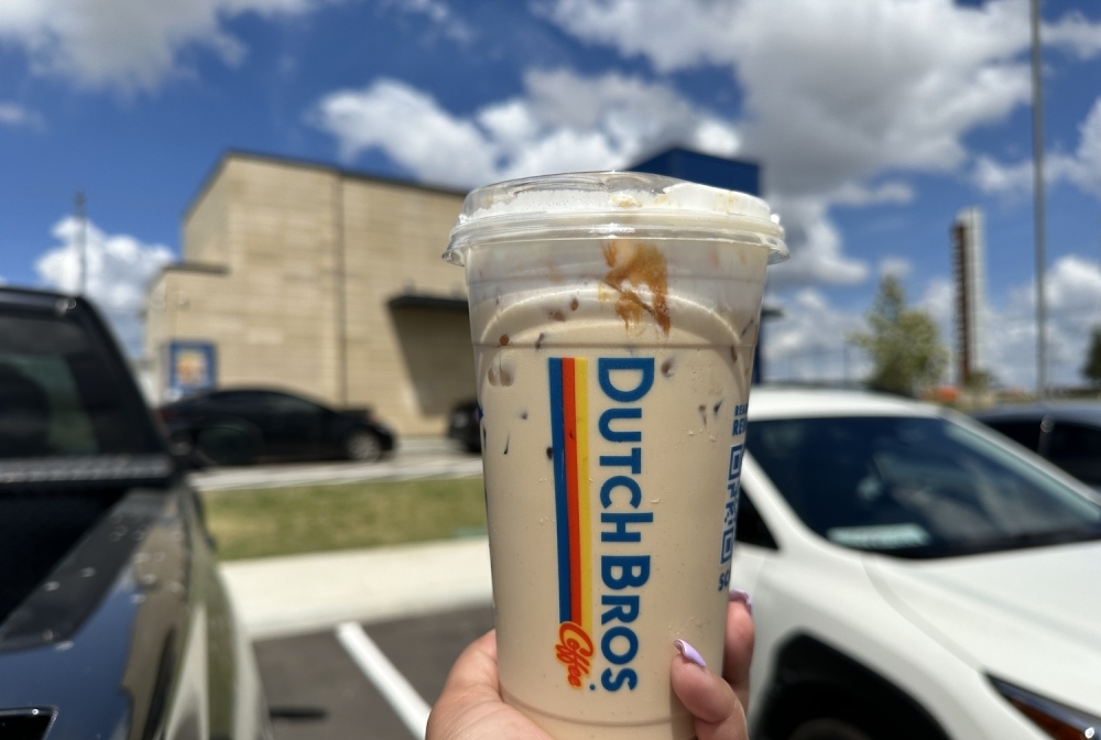The Golden Eagle, a vanilla and caramel breve with caramel drizzle, being held in front of a Dutch Bros location