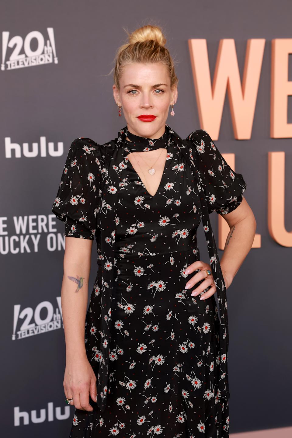 A person poses on the red carpet in a floral-patterned black dress with puffed sleeves and a choker neckline