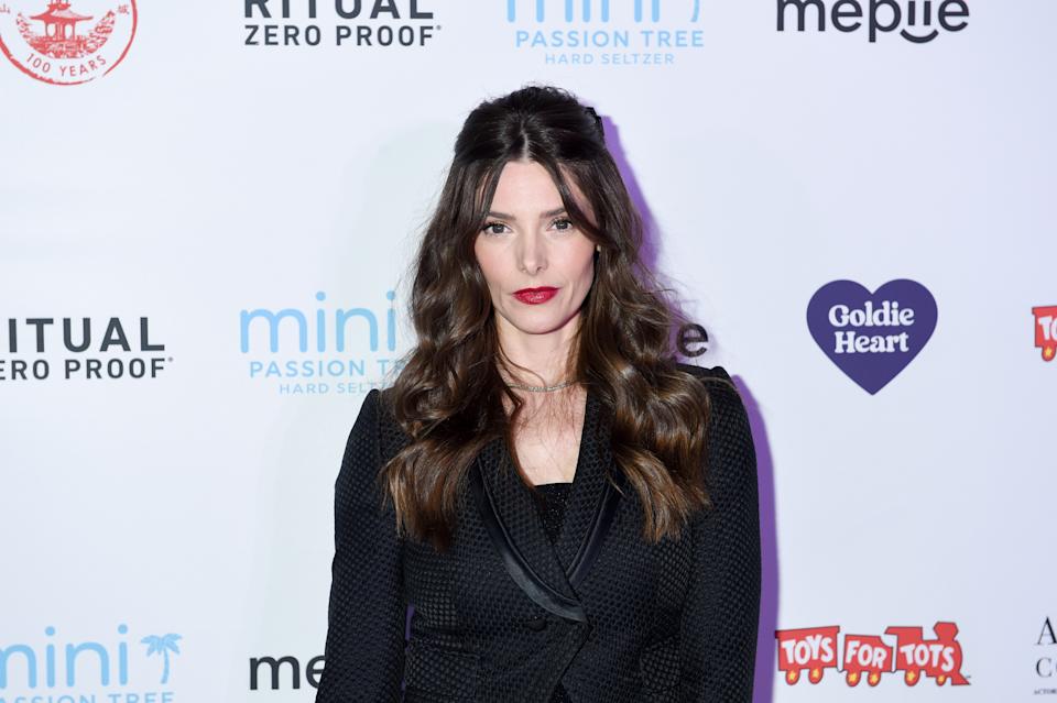 Person in elegant black outfit poses at an event with branded photo background