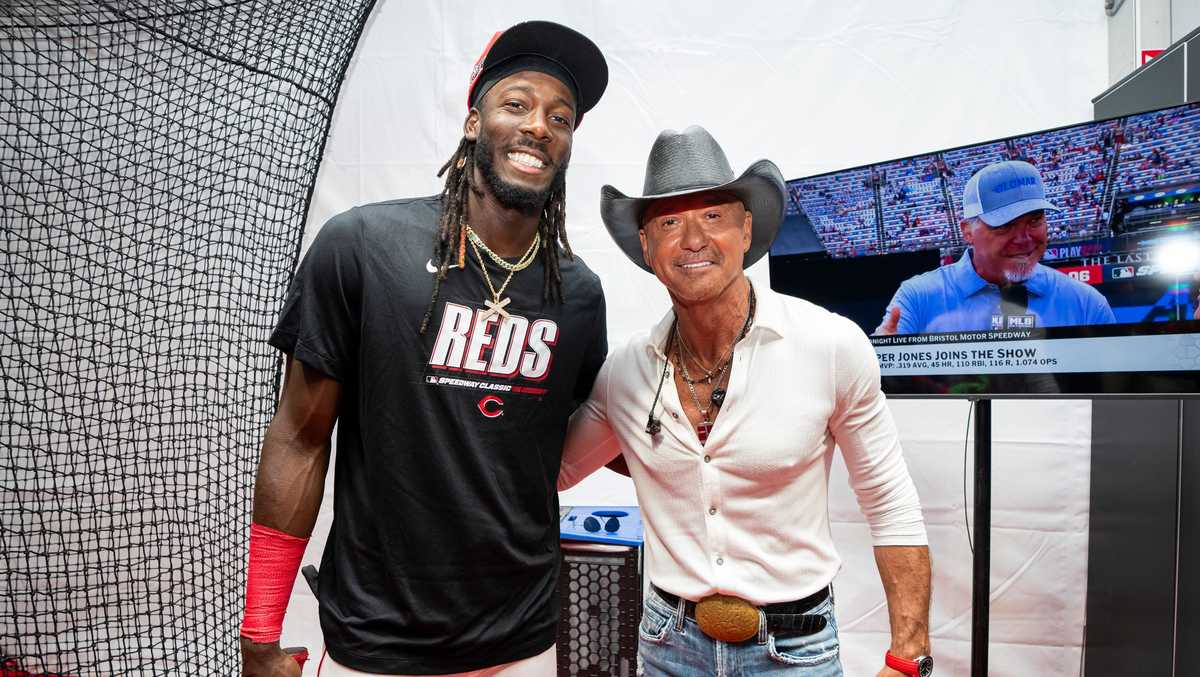 Elly De La Cruz tries his hand at pitching to country star Tim McGraw during Speedway Classic