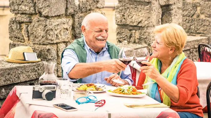 Senior couple having fun and eating at restaurant during travel - Mature man and woman wife in old city town bar during active elderly vacation - Happy retirement concept with retired people together.