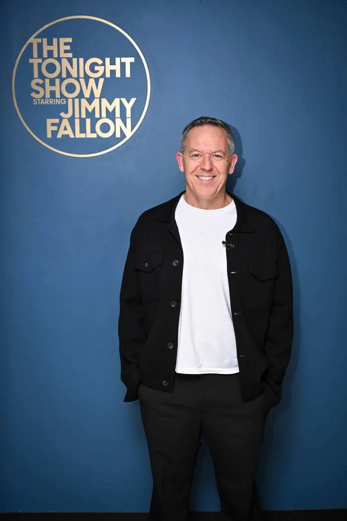 Greg Gutfeld stands smiling on the set of "The Tonight Show Starring Jimmy Fallon," wearing a casual jacket and shirt
