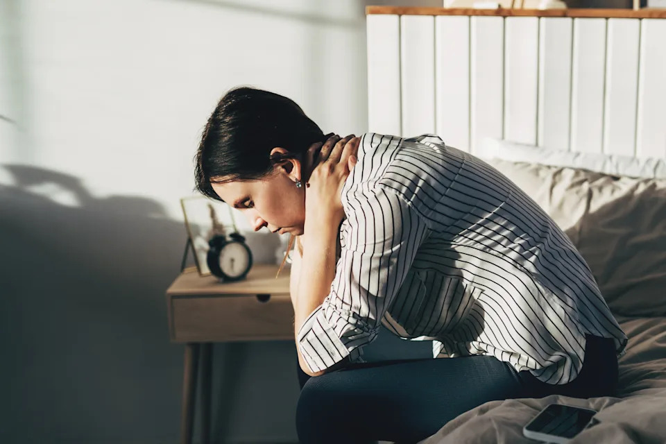 Woman Suffering From Depression Sitting On Bed In Pajamas
