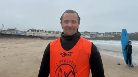 Andrzej Krystowski. He has brown hair, wearing a black wetsuit with orange vest.