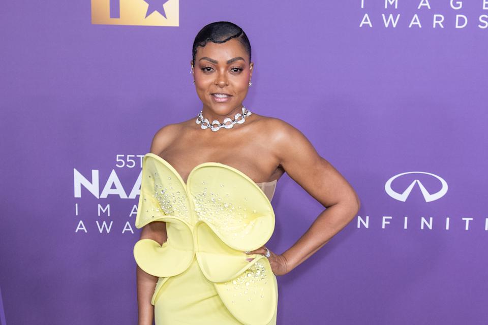 A person in an elegant, strapless gown with unique floral embellishments at an awards event, wearing a sparkling choker necklace
