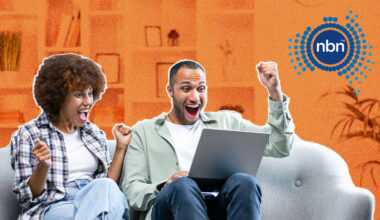 Young couple sitting on a sofa with a laptop and looking excited.