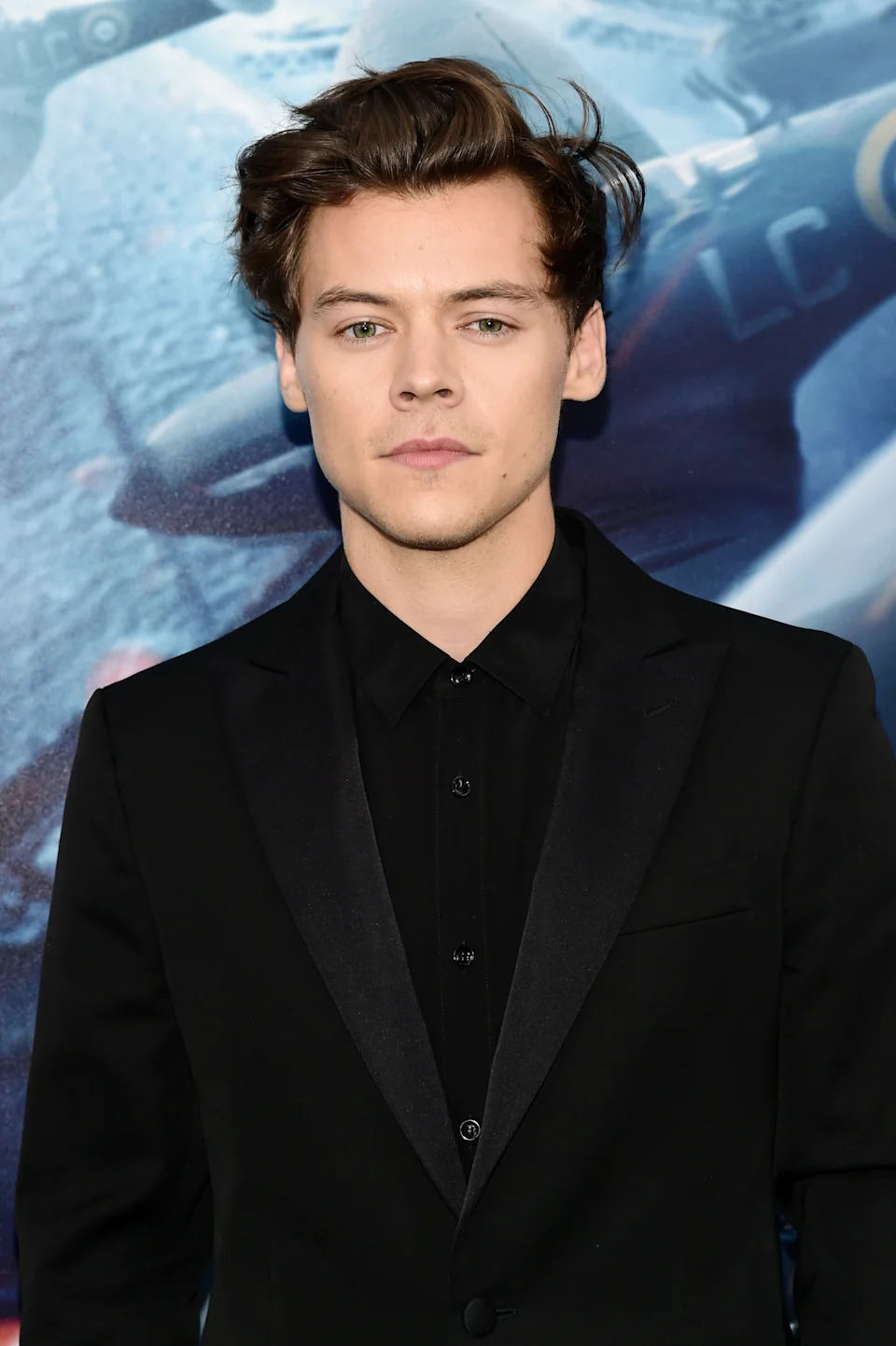 Person in formal, dark suit and shirt at an event, standing in front of a backdrop featuring a movie-themed image
