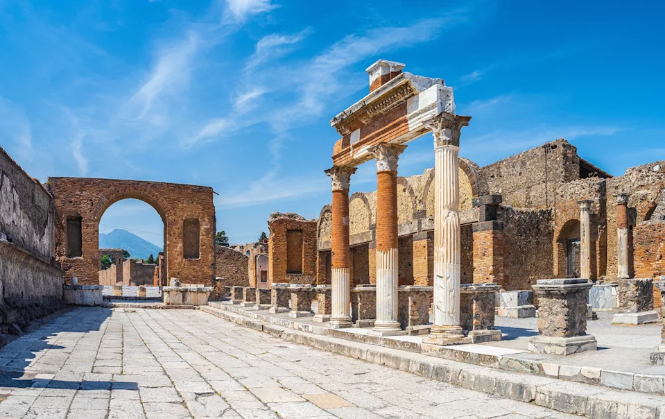 Ancient ruins with columns and arches under a clear sky in Pompeii, showcasing Roman architectural elements and historical significance