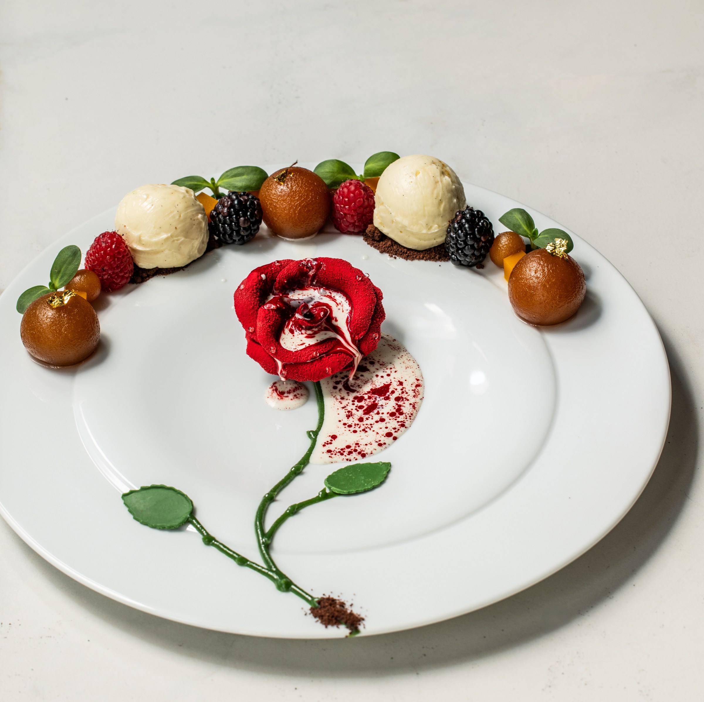 A dessert with a red flower and spheres along the rim of the plate.