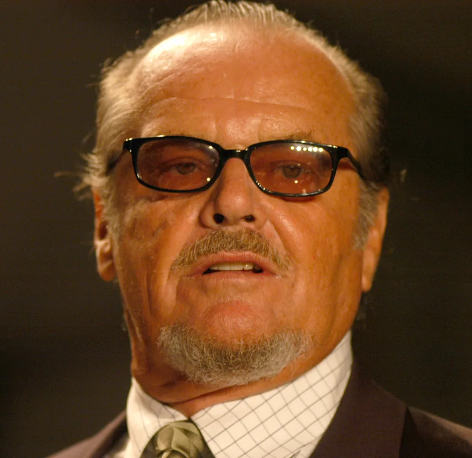 Elderly man with sunglasses and a trimmed goatee, wearing a suit and tie