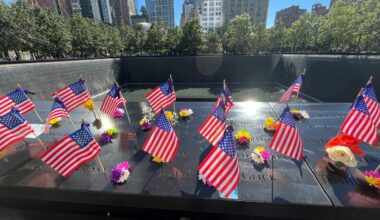 Flags and flowers are placed by the names of those killed during the Sept. 11, 2001, attacks, at the reflecting pools at the National September 11 Memorial & Museum, Tuesday, Sept. 10, 2024, in New York. (AP Photo/Donald King)