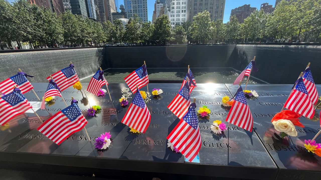 Flags and flowers are placed by the names of those killed during the Sept. 11, 2001, attacks, at the reflecting pools at the National September 11 Memorial & Museum, Tuesday, Sept. 10, 2024, in New York. (AP Photo/Donald King)