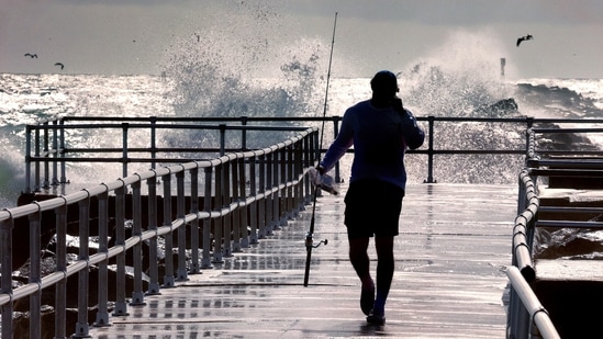 A fisherman walks on a pier as large waves generated by Hurricane Erin crashi into the jetty at Lighthouse Point Park, in Ponce Inlet, Fla., Wednesday, Aug. 20, 2025. (Joe Burbank/Orlando Sentinel via AP)(AP)