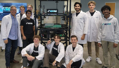 John Lauer (left) and members of the Adom Industries team gather around the company’s “workcell”—the core of its cloud-connected electronics prototyping factory. Lauer likens the system to “compute for atoms,” much like a server in a data center enables “compute for bits,” calling it the Amazon Web Services of electronics prototyping. The photo was taken shortly after a major presentation to a leading electronics company, following months of preparation.