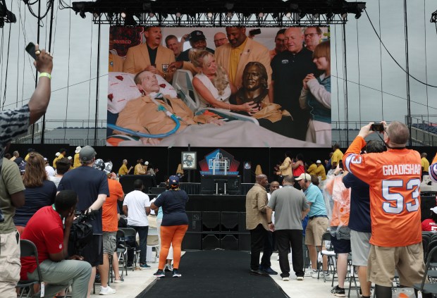 Steve McMichael and his wife, Misty, along with former teammates, are displayed on the video board as he is inducted into the Pro Football Hall of Fame during the enshrinement ceremony at Tom Benson Hall of Fame Stadium on Aug. 3, 2024, in Canton, Ohio. (John J. Kim/Chicago Tribune)